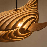 Lampe suspendue baleine en bois naturel, gros plan des rainures sculptées et câble noir, lumière