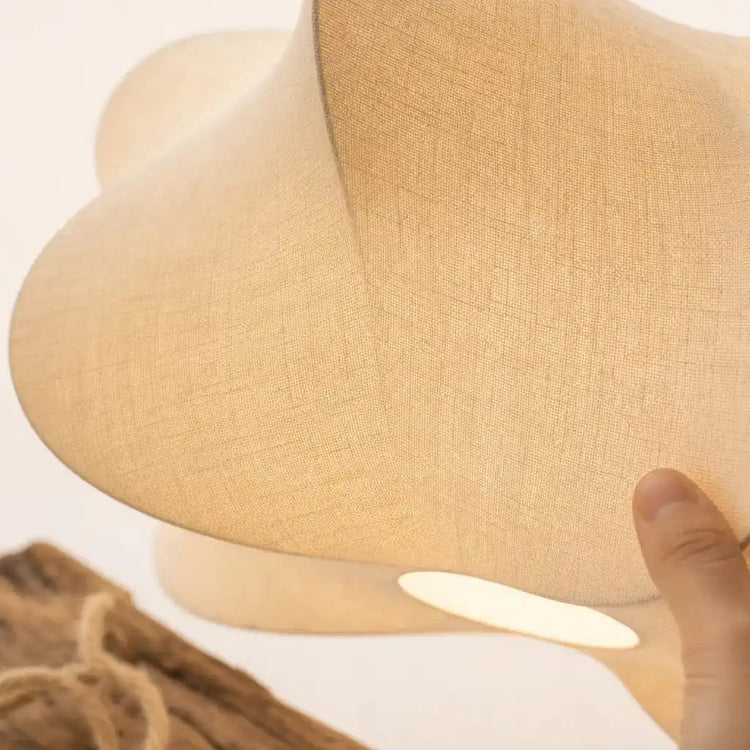 Abat-jour nuage en lin beige, main près de la lampe, lumière sous l’abat-jour