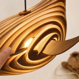 Lampe suspendue baleine en bois naturel, gros plan des rainures sculptées, main