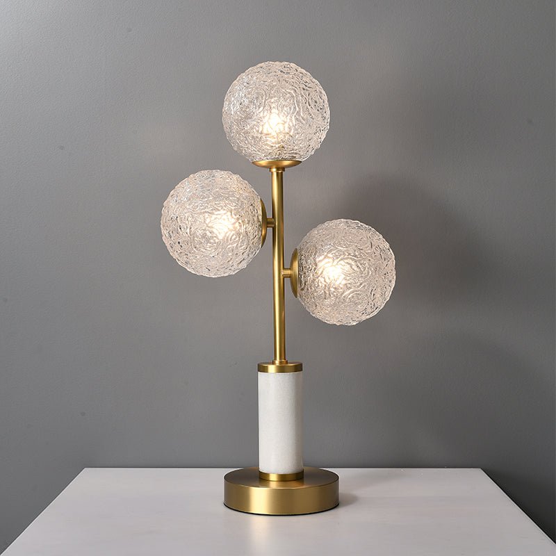 Lampe à poser 3 lumières : trois globes en verre texturé sur tige laiton, socle blanc et base dorée.