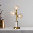 Lampe à poser 3 lumières : trois globes en verre texturé, monture laiton, base ronde dorée.