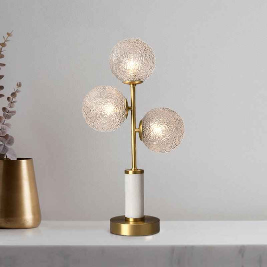 Lampe à poser 3 lumières : trois globes en verre texturé, monture laiton, base ronde dorée.