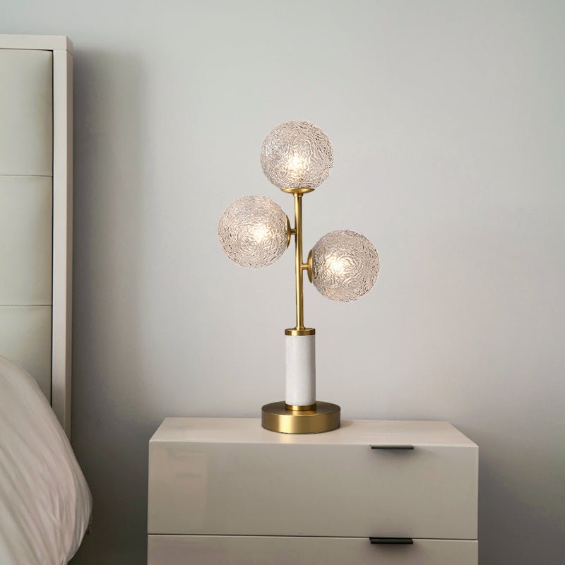 Lampe à poser 3 lumières avec trois globes en verre texturé, pied laiton et socle cylindrique blanc.