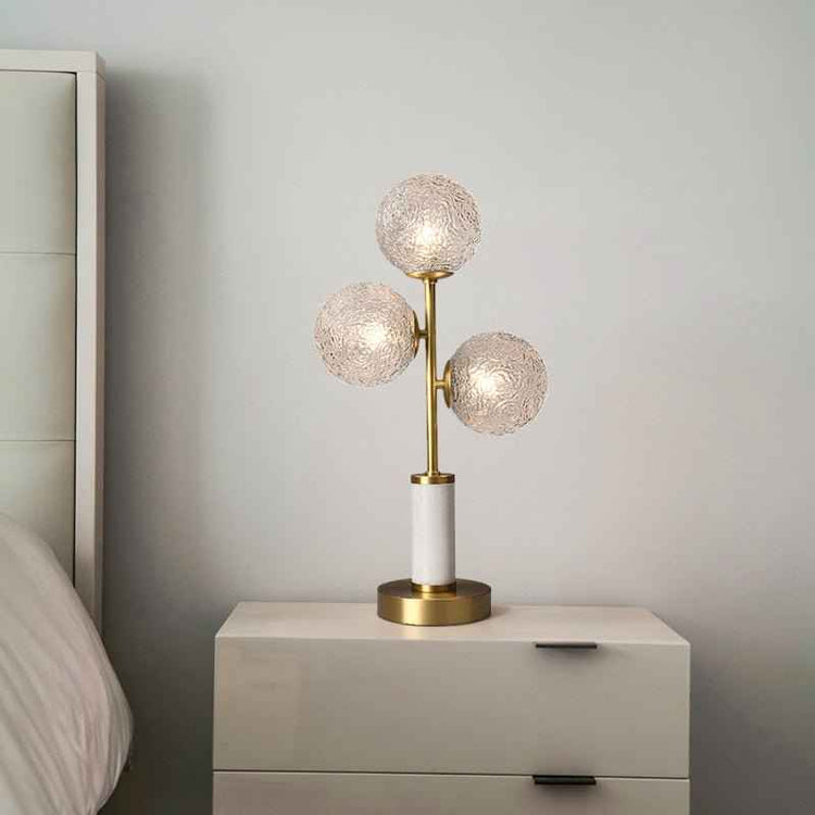 Lampe à poser 3 lumières avec trois globes en verre texturé, pied laiton et socle cylindrique blanc.
