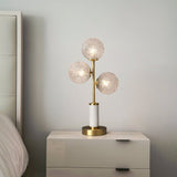 Lampe à poser 3 lumières avec trois globes en verre texturé, pied laiton et socle cylindrique blanc.