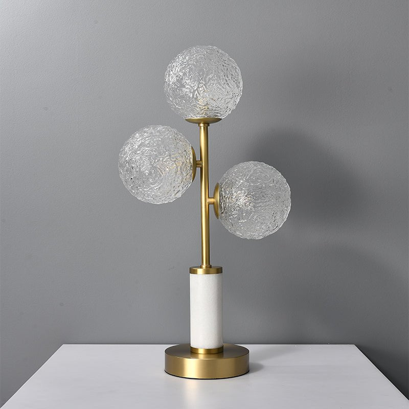 Lampe à poser 3 lumières avec trois globes en verre texturé, monture laiton, socle cylindrique blanc.
