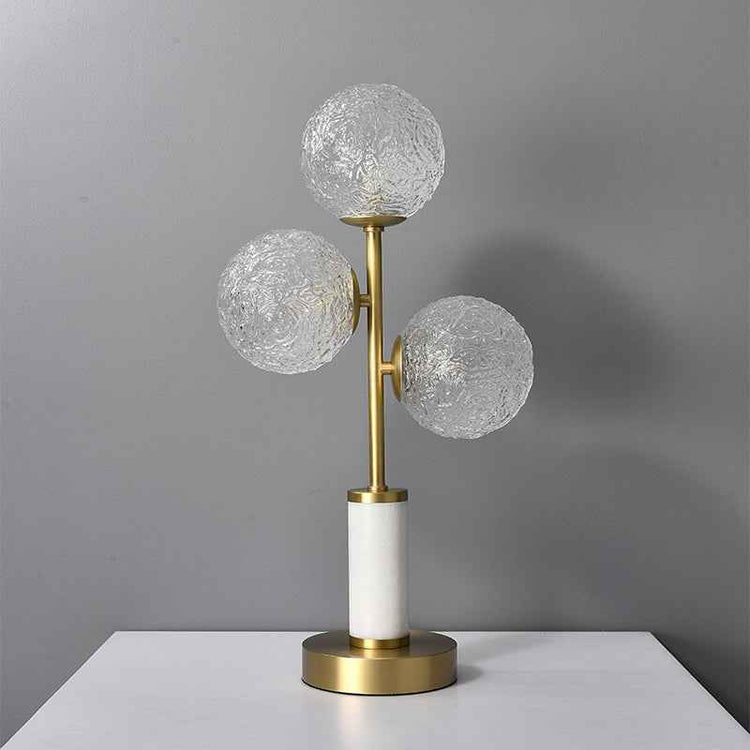 Lampe à poser 3 lumières avec trois globes en verre texturé, monture laiton, socle cylindrique blanc.
