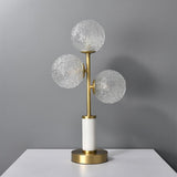 Lampe à poser 3 lumières avec trois globes en verre texturé, monture laiton, socle cylindrique blanc.