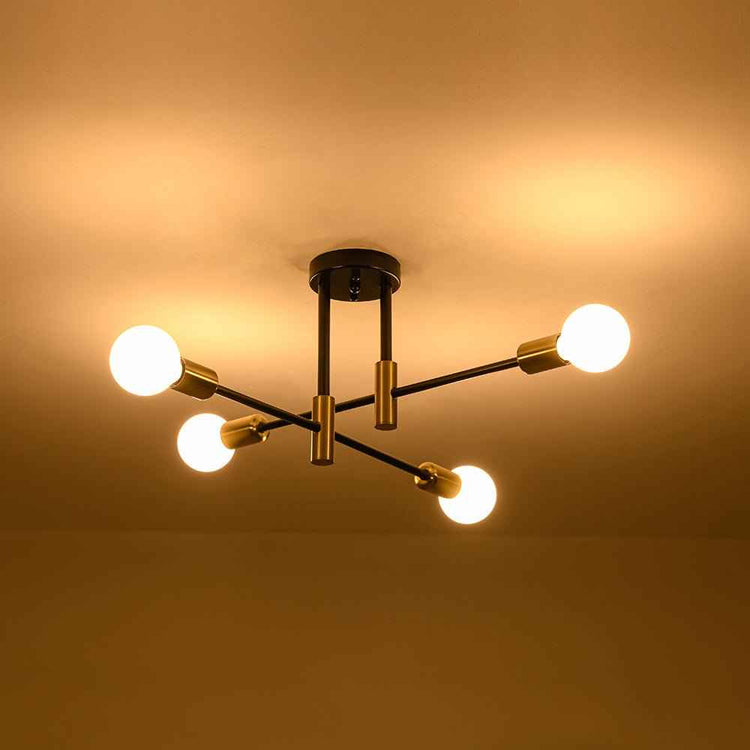 Plafonnier sputnik 4 lumières noir et laiton, ampoules allumées, bras croisés.