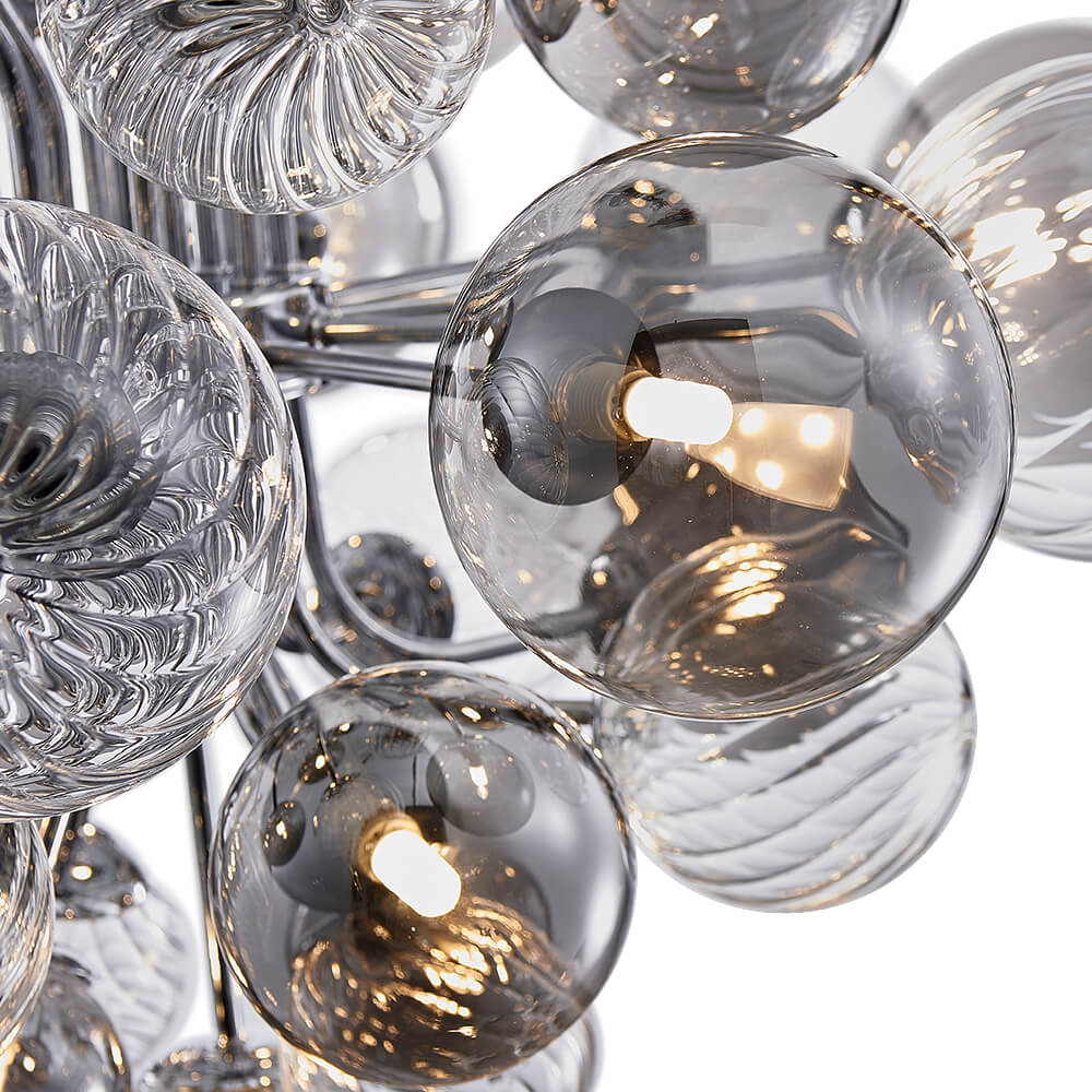 Détail du lustre : boules de verre fumé avec ampoules allumées et bras chromés.
