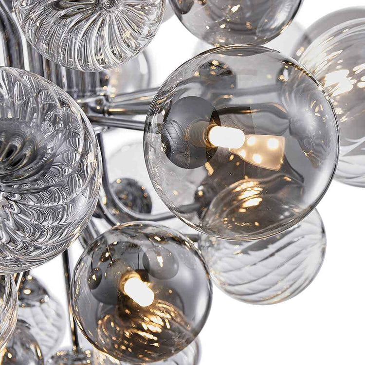 Détail du lustre : boules de verre fumé avec ampoules allumées et bras chromés.