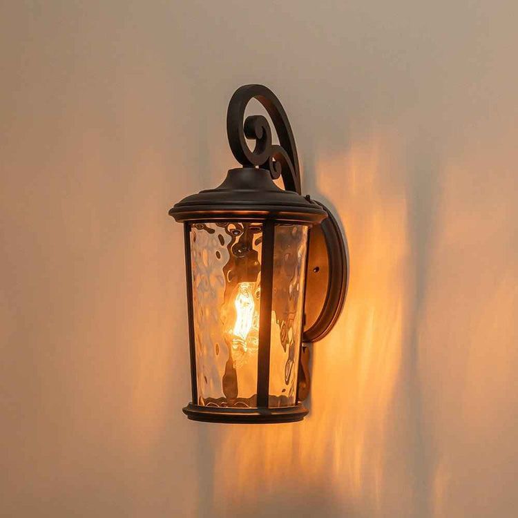 Applique extérieure lanterne IP23 allumée : métal noir et verre transparent.