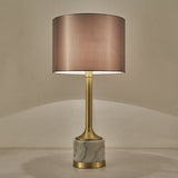 Lampe à poser à abat-jour en tissu beige rosé, pied doré et base en marbre blanc veinuré.