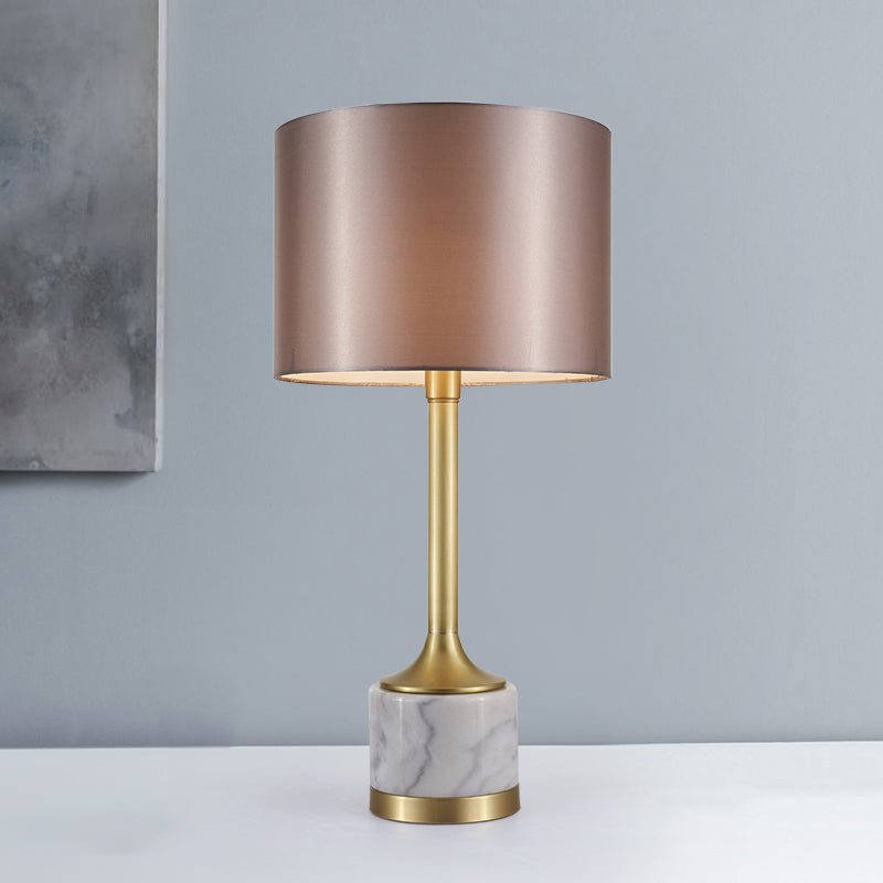 Lampe à poser : abat-jour en tissu beige rosé, pied en marbre blanc veinuré et base dorée.
