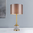 Lampe à poser : abat-jour en tissu beige rosé, pied en marbre blanc veinuré et base dorée.