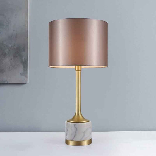 Lampe à poser : abat-jour en tissu beige rosé, pied en marbre blanc veinuré et base dorée.