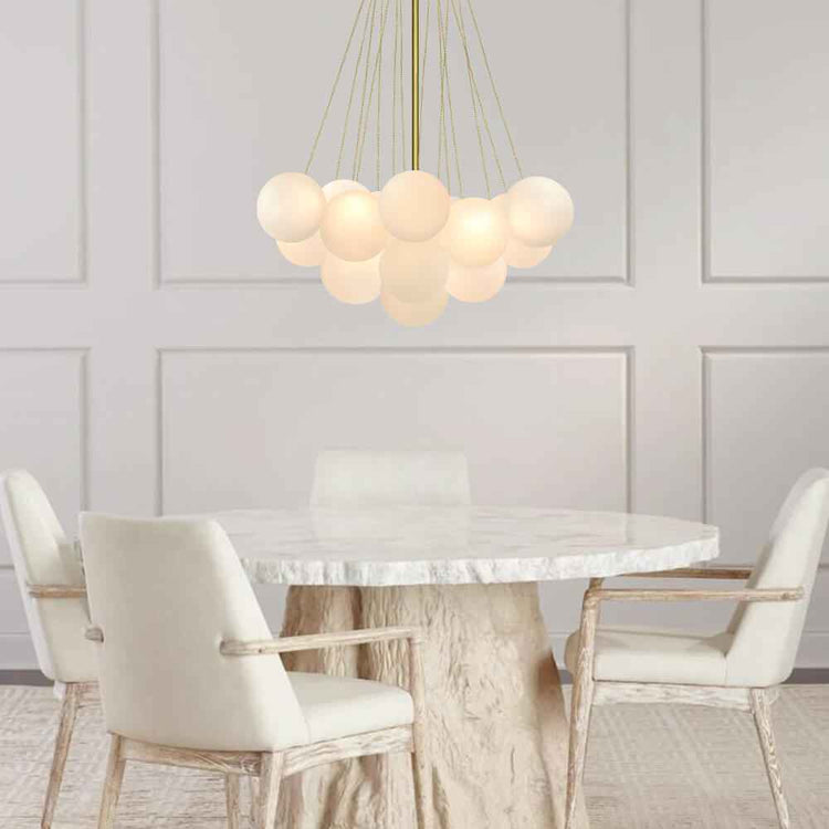 Lustre suspendu moderne à boules en verre blanc en grappe, monture dorée au-dessus d’une table.