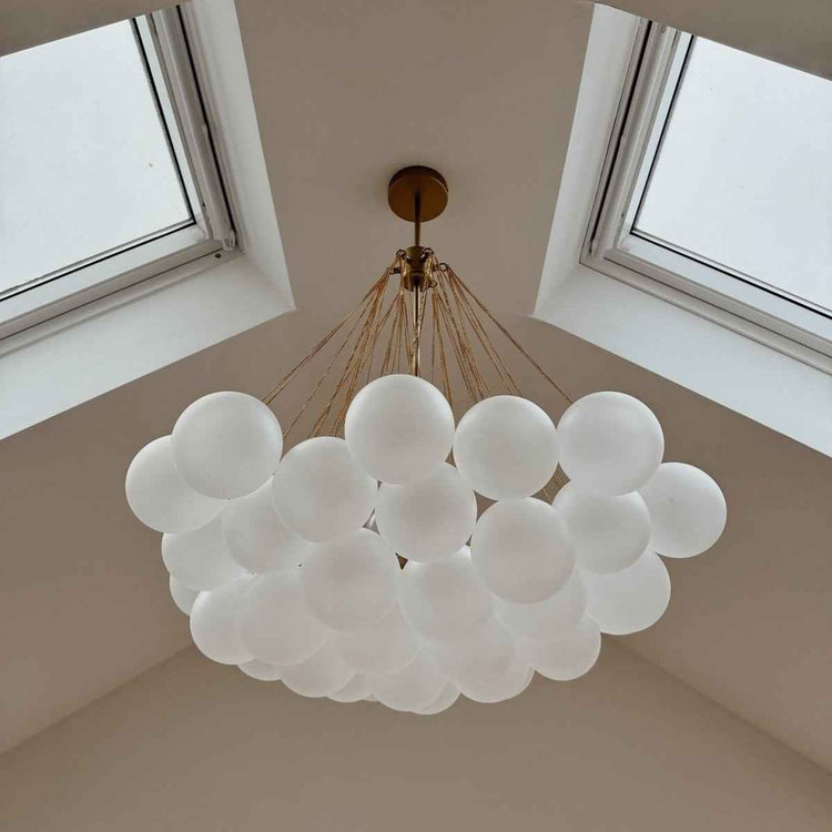 Lustre dans une verrière avec boules en verre blanc, monture dorée et fils fins.