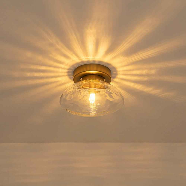 Plafonnier ovale en verre transparent, monture laiton, ampoule allumée au plafond.