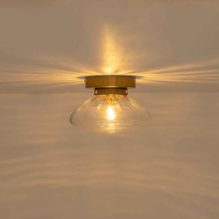 Plafonnier ovale en verre transparent et monture laiton, ampoule allumée.