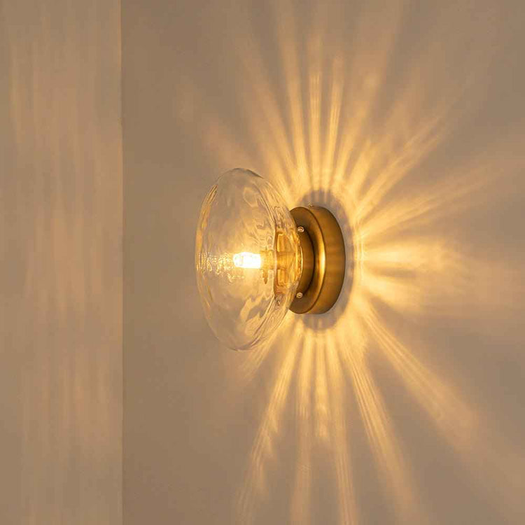 Luminaire ovale en verre transparent avec monture laiton, ampoule allumée.
