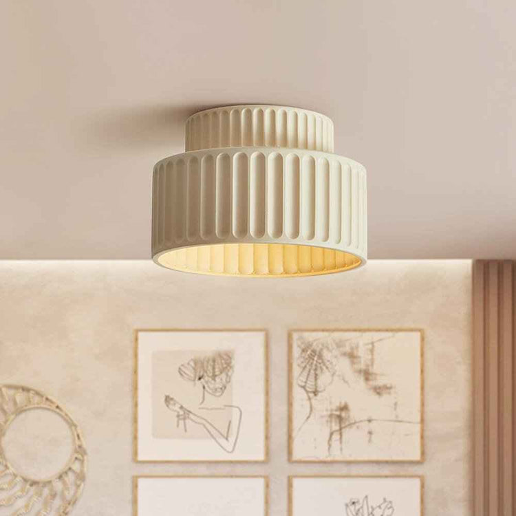 Plafonnier crème en céramique, abat-jour strié à deux étages, lumière chaude visible.