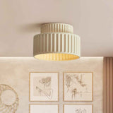 Plafonnier crème en céramique, abat-jour strié à deux étages, lumière chaude visible.