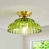 Plafonnier dôme en verre vert nervuré, avec base dorée et ampoule visible.
